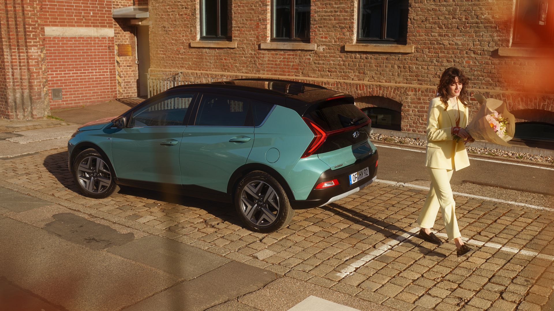 Woman in yellow walking away from the parked all-new Hyundai BAYON compact crossover SUV.